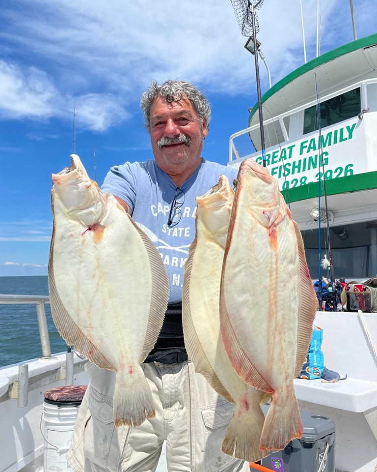 Happy angler with two big fluke on Celtic Quest, Great Family Fishing sign visible