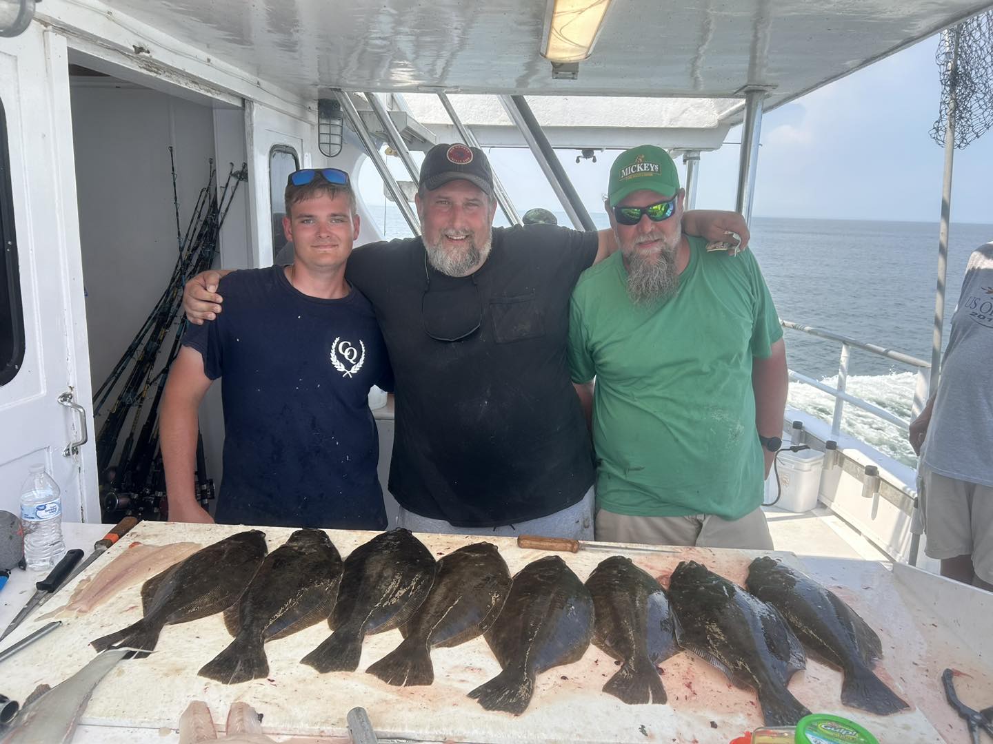 Three men with spread of fluke on cutting board, Celtic Quest fishing charter